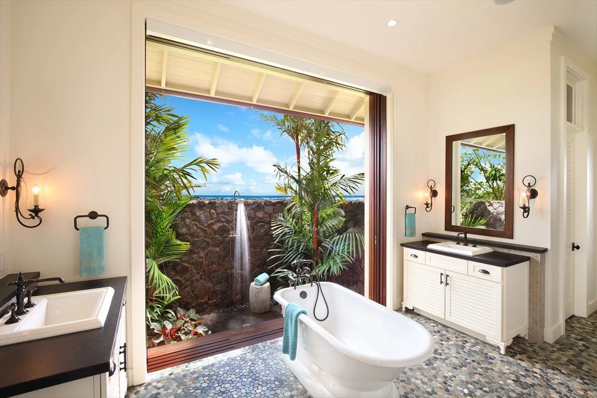 A resort-home bathroom with a freestanding tub and folding lanai doors thrown open to a private outdoor shower and ocean view.
