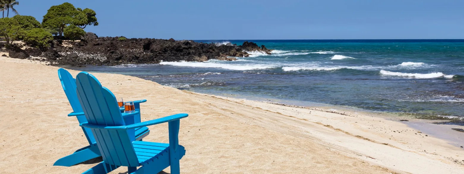Two blue Adirondack chairs on golden sand facing turquoise, white-capped surf under a clear sky.