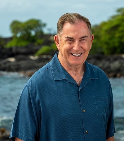 Stephen Proski, smiling, in a blue aloha shirt on a lava-rock stretch of the Kona coastline.